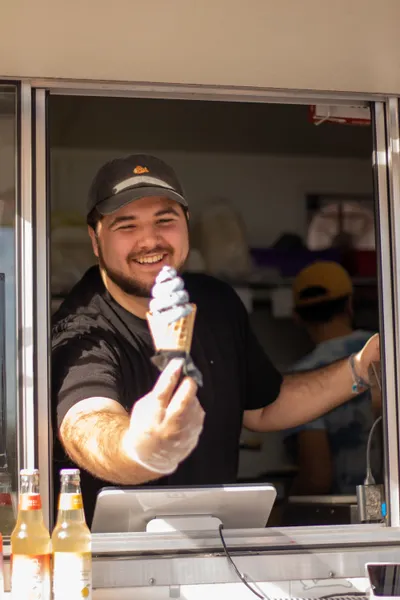 A man handing an ice cream cone to someone from his food truck window.